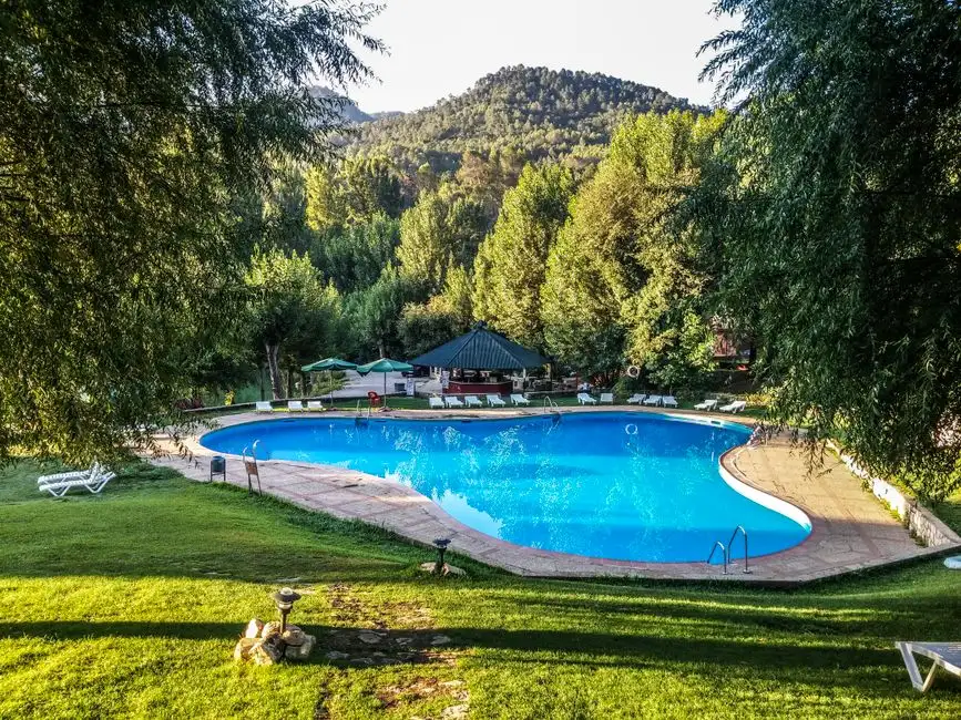 Relax at a luxury resort pool surrounded by lush greenery and scenic hills in Jaén, Spain.