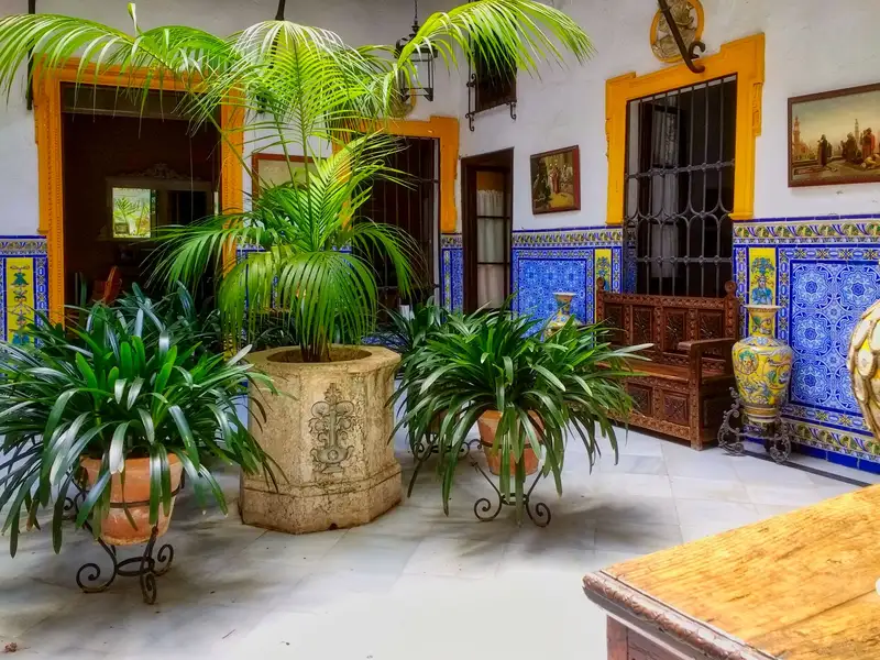 A beautiful Andalusian patio in Seville, featuring traditional tiles and lush green plants in a serene setting.