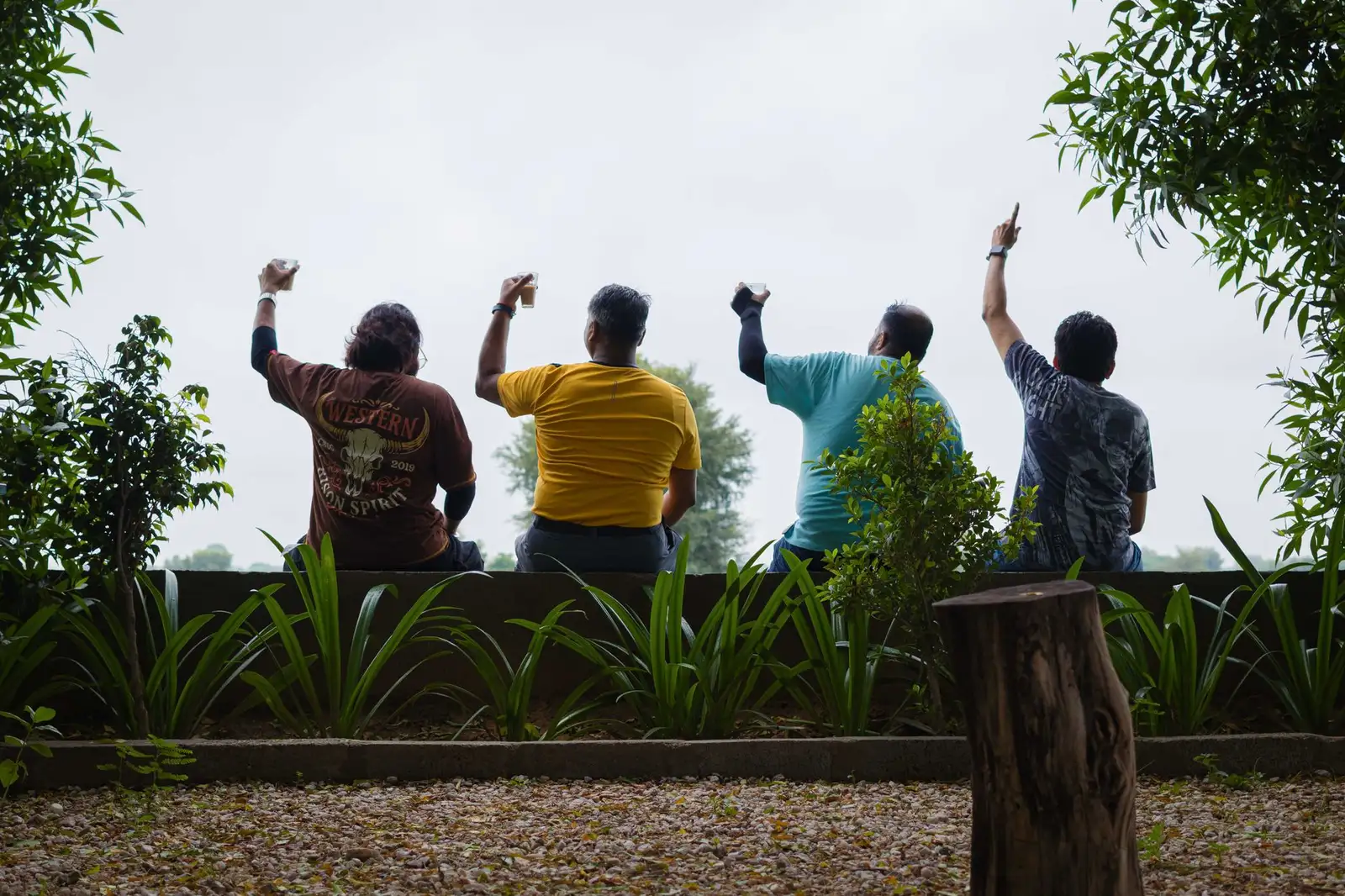 Four people sitting outdoors enjoying nature with raised arms in a relaxed setting.