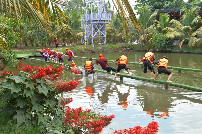 A group of adults crossing a water obstacle course in an outdoor team building exercise.