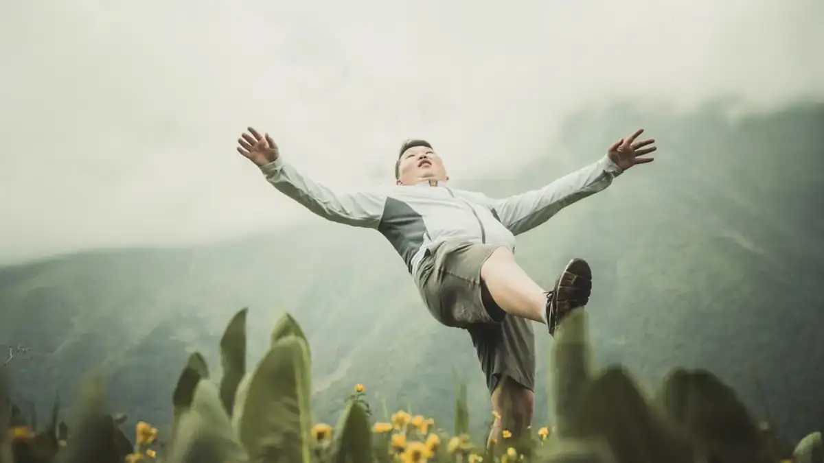 Joyful woman in white long-sleeve shirt and black pants jumps energetically on lush green grass field during daytime corporate retreat